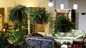 Ein gemütlicher Innenraum mit hängenden Pflanzen, einem floralen Sofa und einem Essbereich mit Stühlen und Tischen.