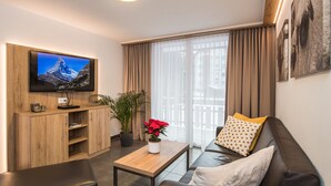 Un salon moderne avec un téléviseur à écran plat, des meubles en bois, une table basse ornée d’une plante en pot et un canapé en cuir.