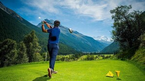 Une personne jouant au golf sur un terrain bien entretenu, avec une chaîne de montagnes en arrière-plan.