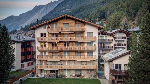 Un hôtel à plusieurs étages, doté de balcons, d’une façade en pierre et surplombant un paysage montagneux.