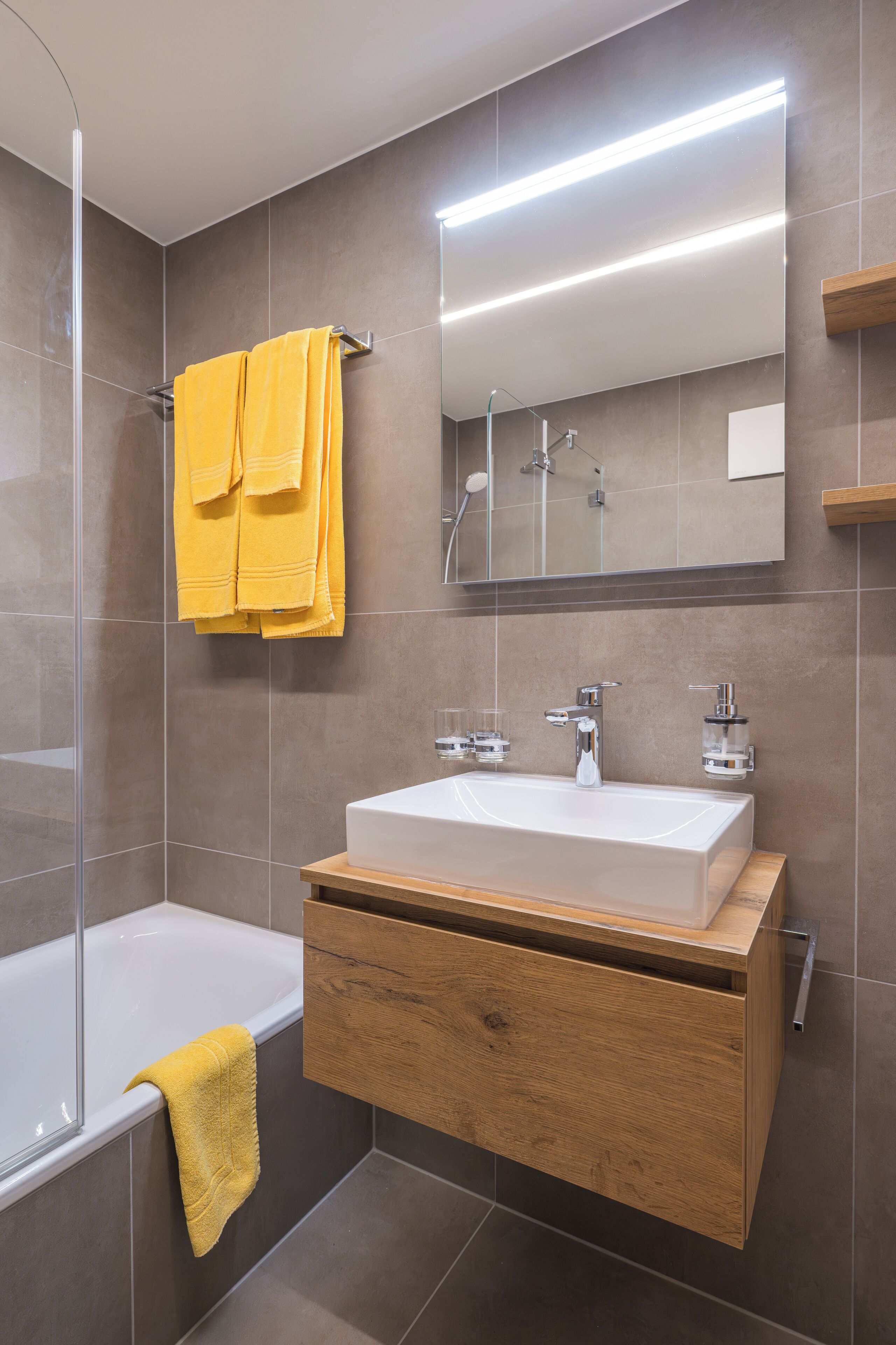 A modern bathroom with a large white sink, wooden vanity, and a glass shower enclosure.