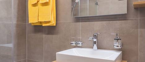 A modern bathroom with a large white sink, wooden vanity, and a glass shower enclosure.