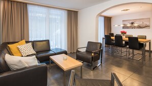 Un salon moderne avec un canapé, un fauteuil et une petite table. On y trouve également un coin repas avec une table et des chaises.