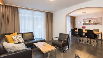 Un salon moderne avec un canapé, un fauteuil et une petite table. On y trouve également un coin repas avec une table et des chaises.