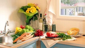 A kitchen with a sink, countertop, and various vegetables like carrots and tomatoes.