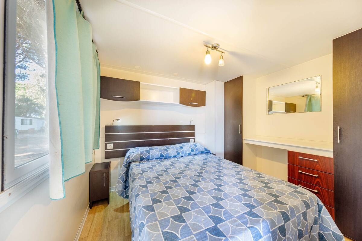 A bedroom with a bed, a window with curtains, a mirror, and a wardrobe.