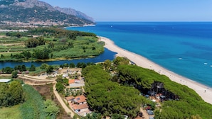 An aerial view of a coastal area with a beach, a river, and a mountainous backdrop.