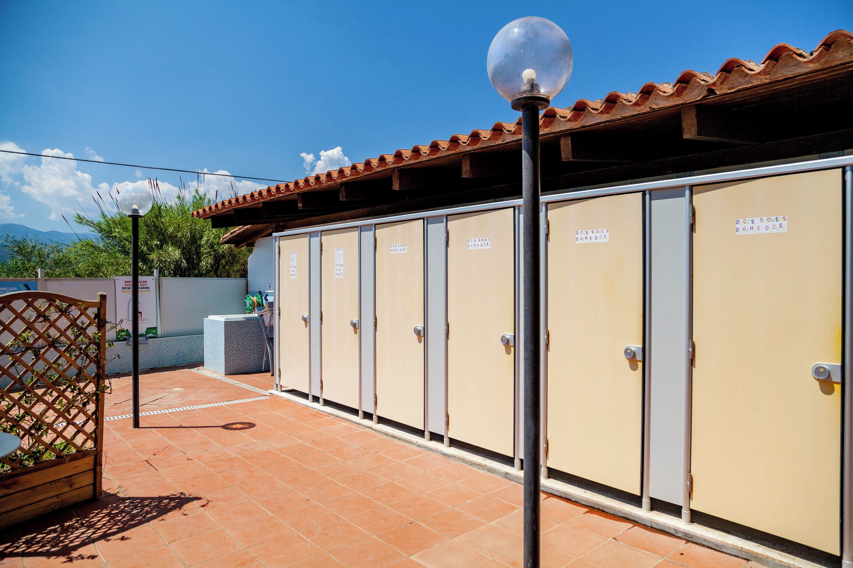 Une rangée de casiers beiges avec des poignées en métal, un ciel dégagé et une terrasse carrelée avec une clôture en bois et un lampadaire.