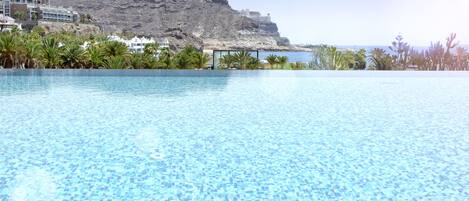 Una piscina azul cristalina con vistas a una montaña y edificios al fondo.