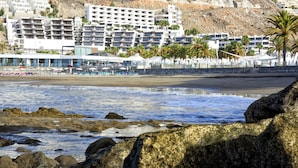 Un hôtel situé en bord de mer, doté de nombreux balcons, de palmiers et d’une côte rocheuse.