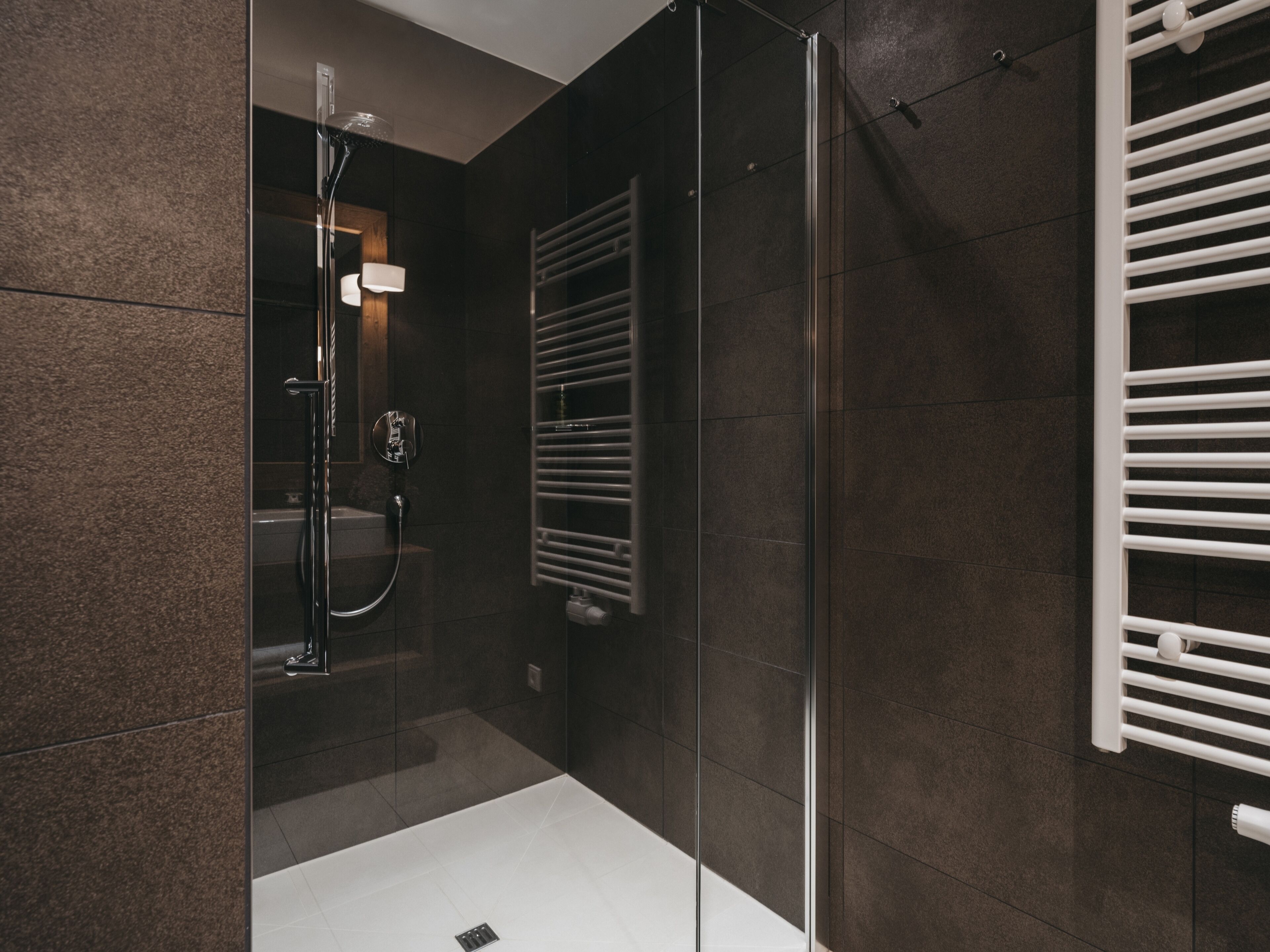 Un baño moderno con ducha envuelta en cristal, un lavamanos blanco y un perchero para toallas.