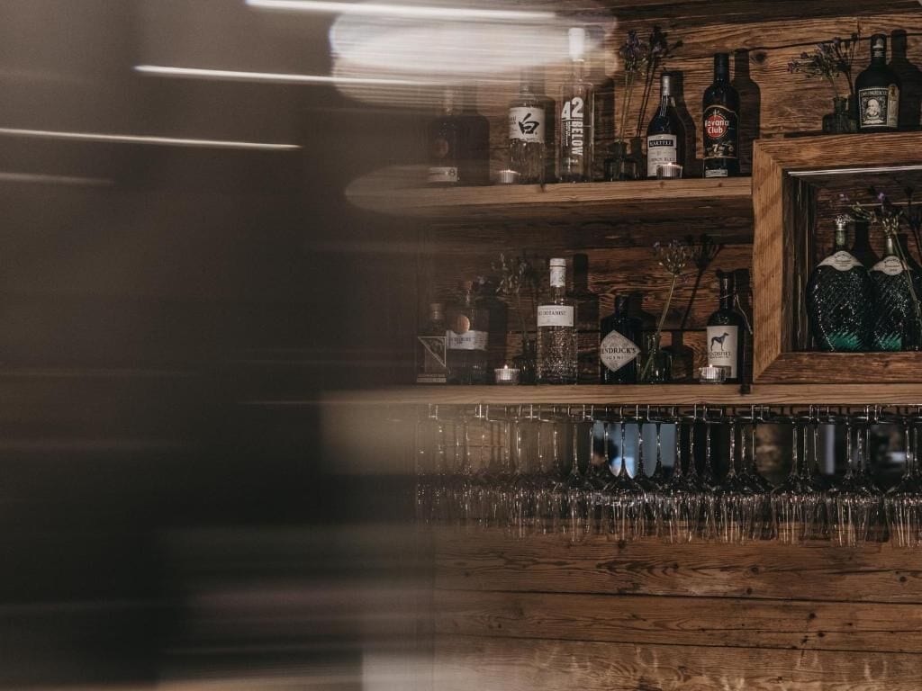 A bar area with shelves of liquor bottles and a row of glasses.