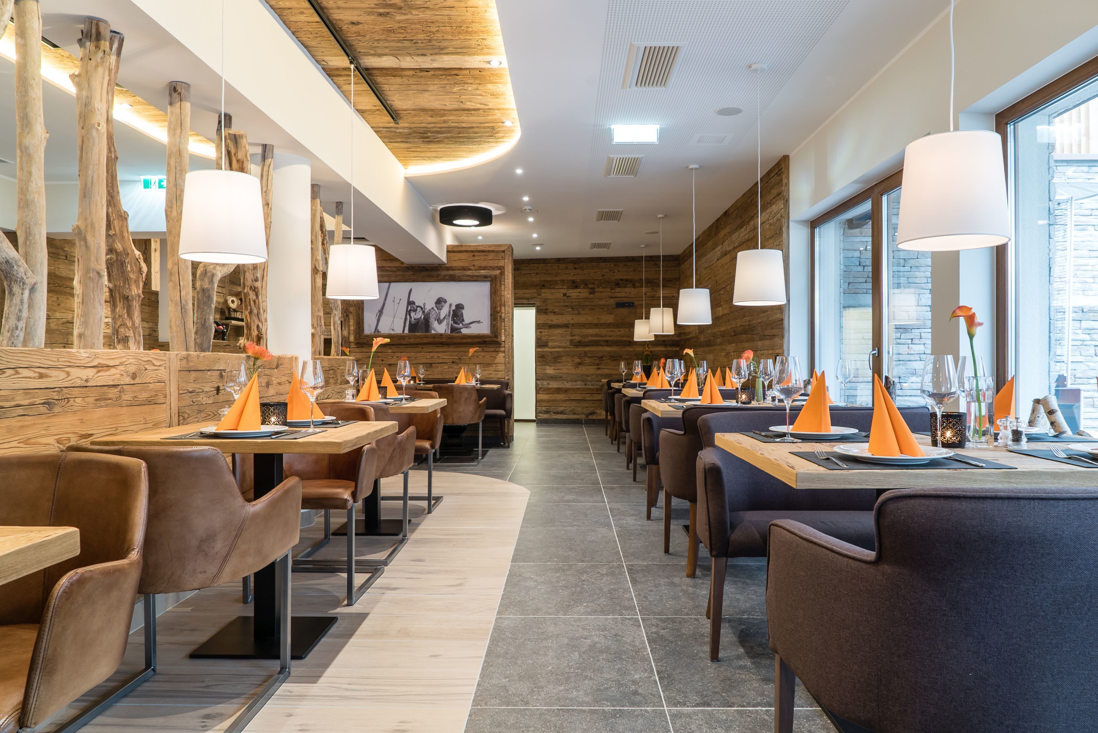Een modern restaurant met houten details, lange tafels en oranje servet houders.