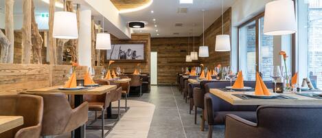 Een modern restaurant met houten details, lange tafels en oranje servet houders.