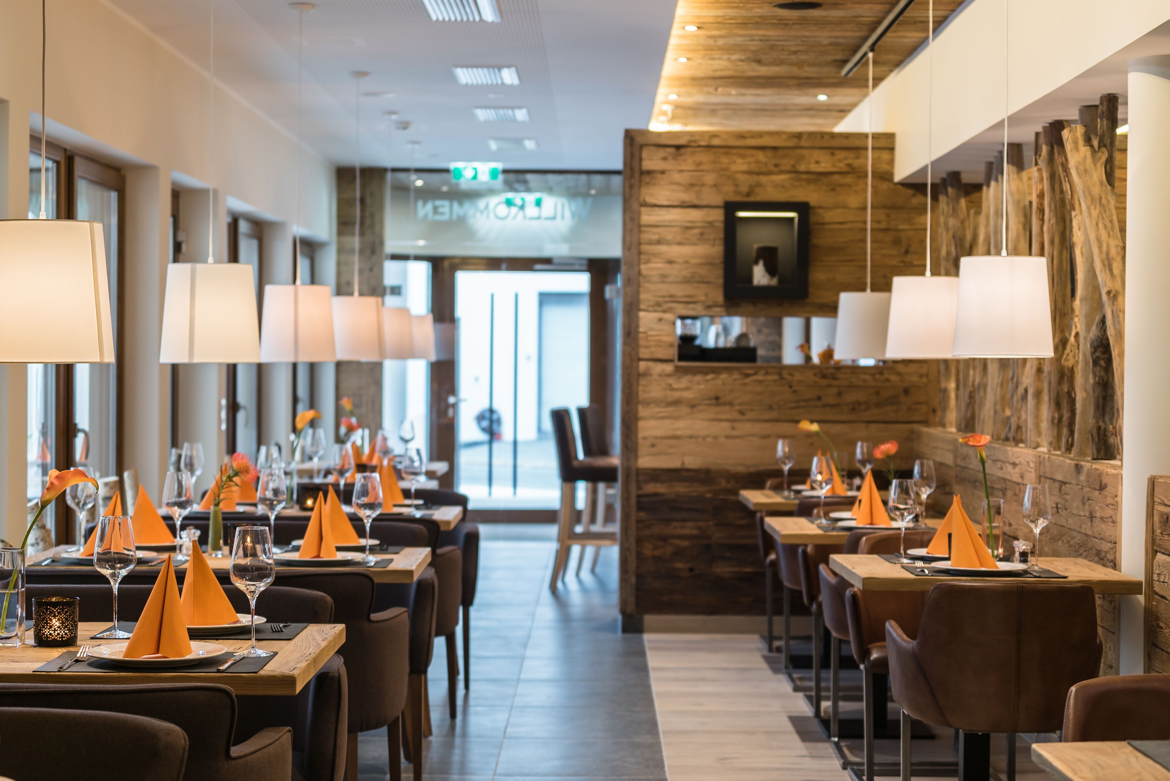 Restaurante com mesas preparadas para refeições, apresentando um interior moderno com detalhes em madeira e iluminação pendente.