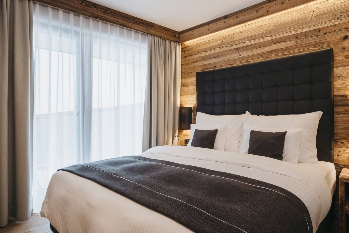 Habitación de hotel moderna con una cama grande, pared de paneles de madera y un amplio ventanal con cortinas.