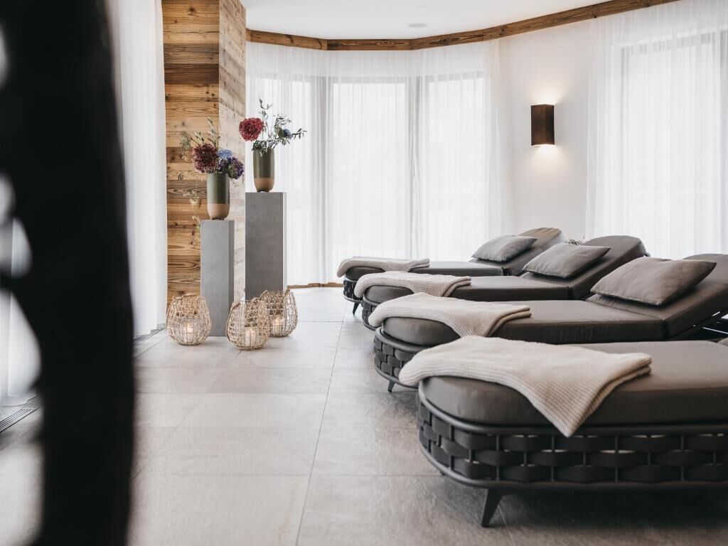 Un cuarto de spa con tres sillas de masaje, una pared de madera, un ventanal con cortinas translúcidas y un jarrón con flores.