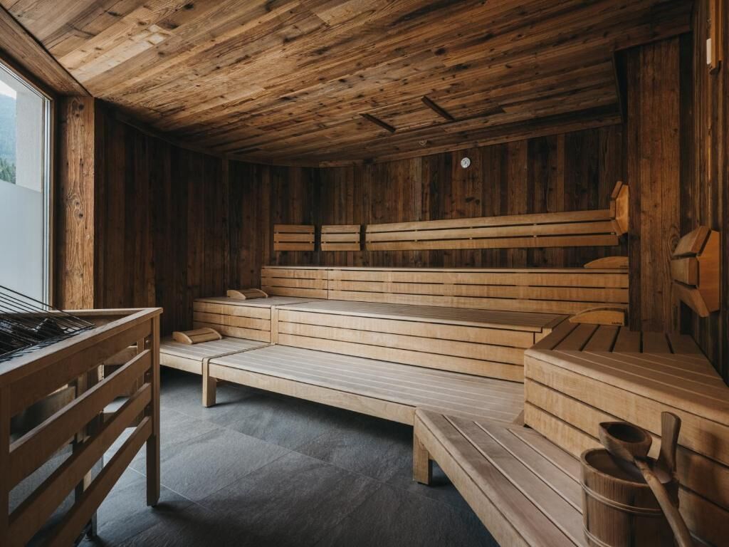 Una sauna de madera con bancos y un asiento de banco, una mesa de madera y un cubo.