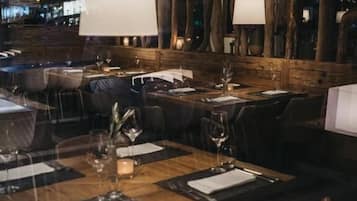 Un restaurante con mesas y sillas de madera, grandes lámparas colgantes y vistas a la ciudad iluminada de noche.