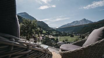 Una silla de mimbre y una mesa en un balcón con vistas a un paisaje montañoso bajo un cielo despejado.