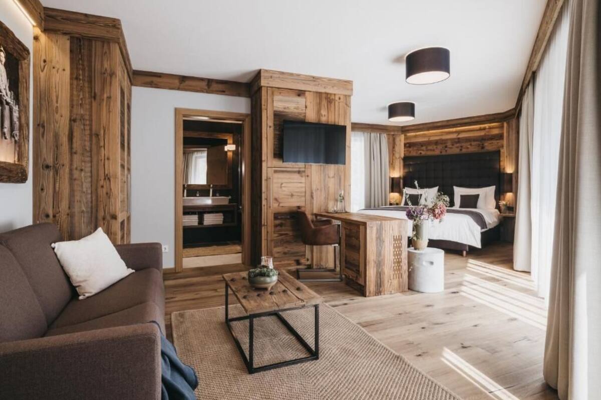 Un salón moderno con un sofá, una mesa de centro y una zona de comedor con una mesa y sillas. Se ve una cama con cabecera al fondo.