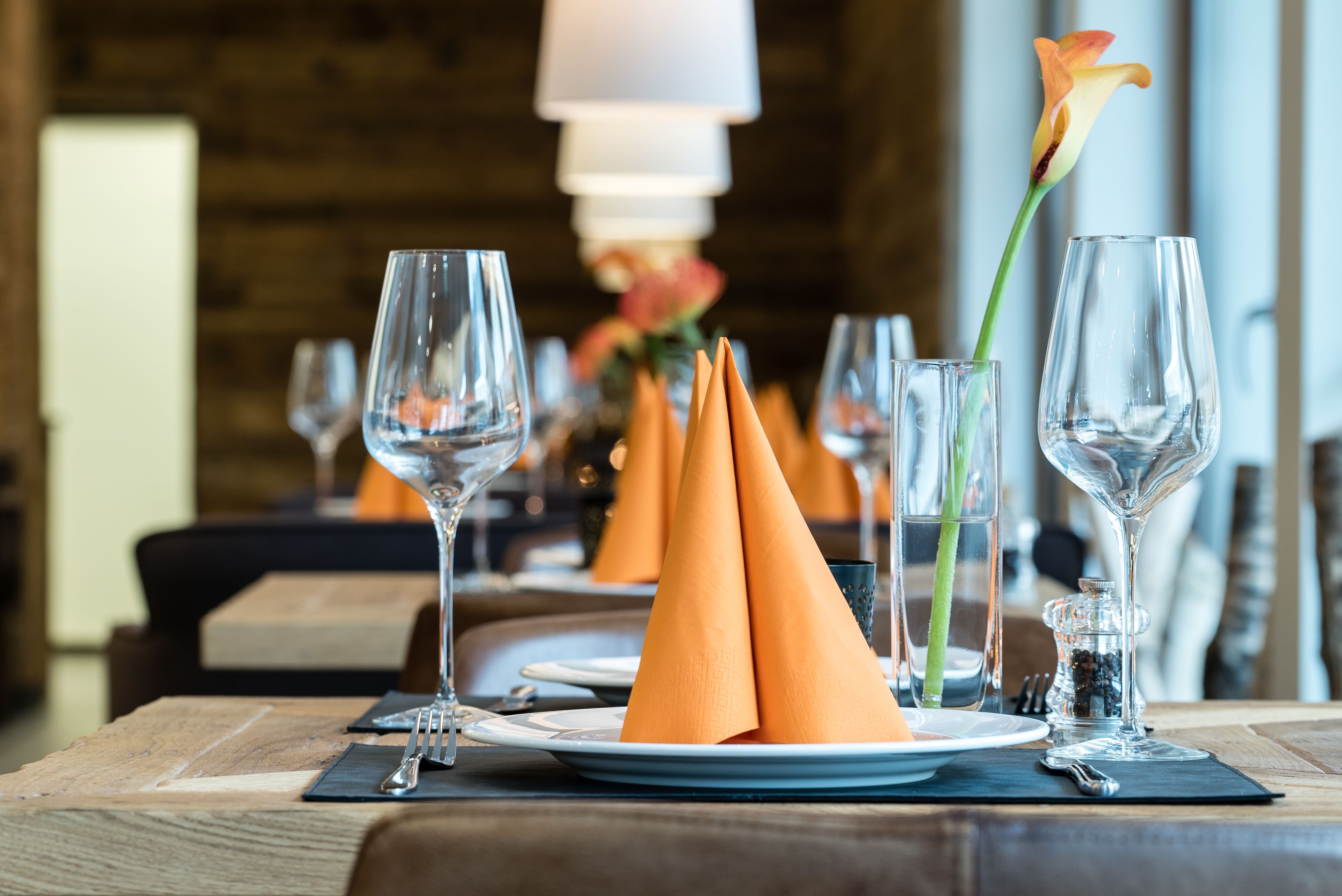 A dining table set with plates, glasses, and orange napkins.