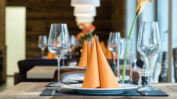 A dining table set with plates, glasses, and orange napkins.