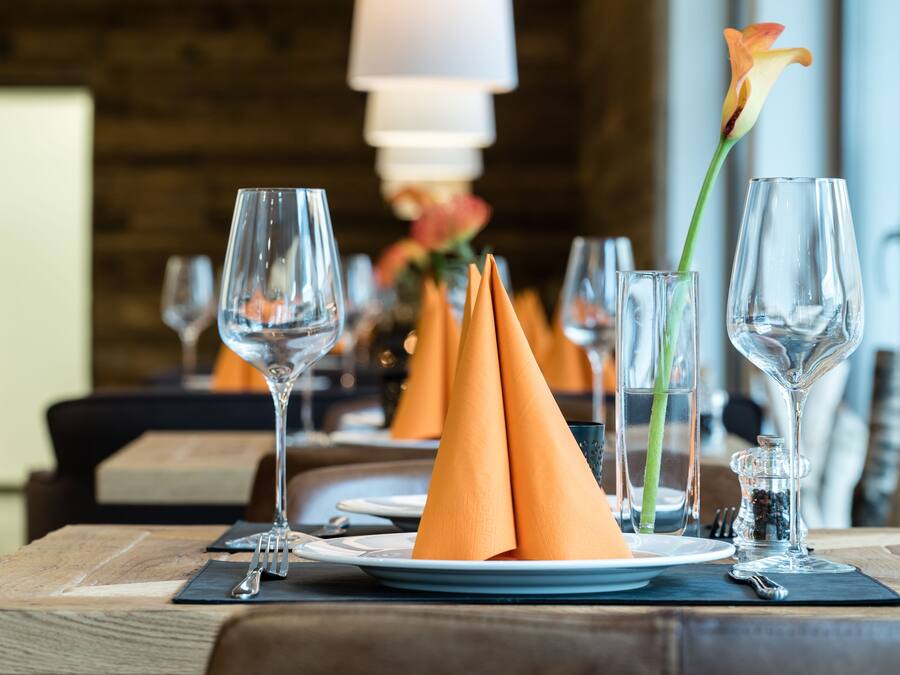 A dining table set with plates, glasses, and orange napkins.