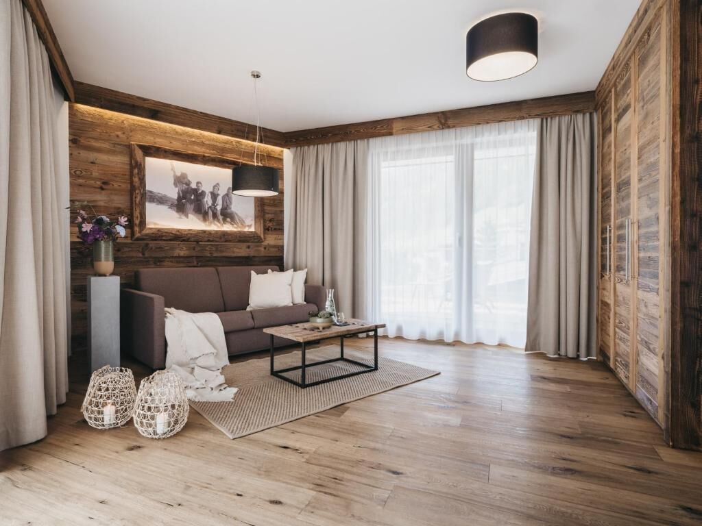 A modern living room with a wooden floor, a brown sofa, a coffee table, and a large window with sheer curtains.