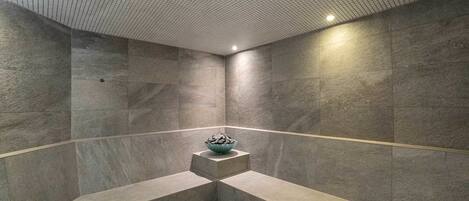 Un baño moderno con una bañera grande y rectangular, un lavamanos pequeño con un cuenco de piedras y un techo con diseño de cuadrícula.