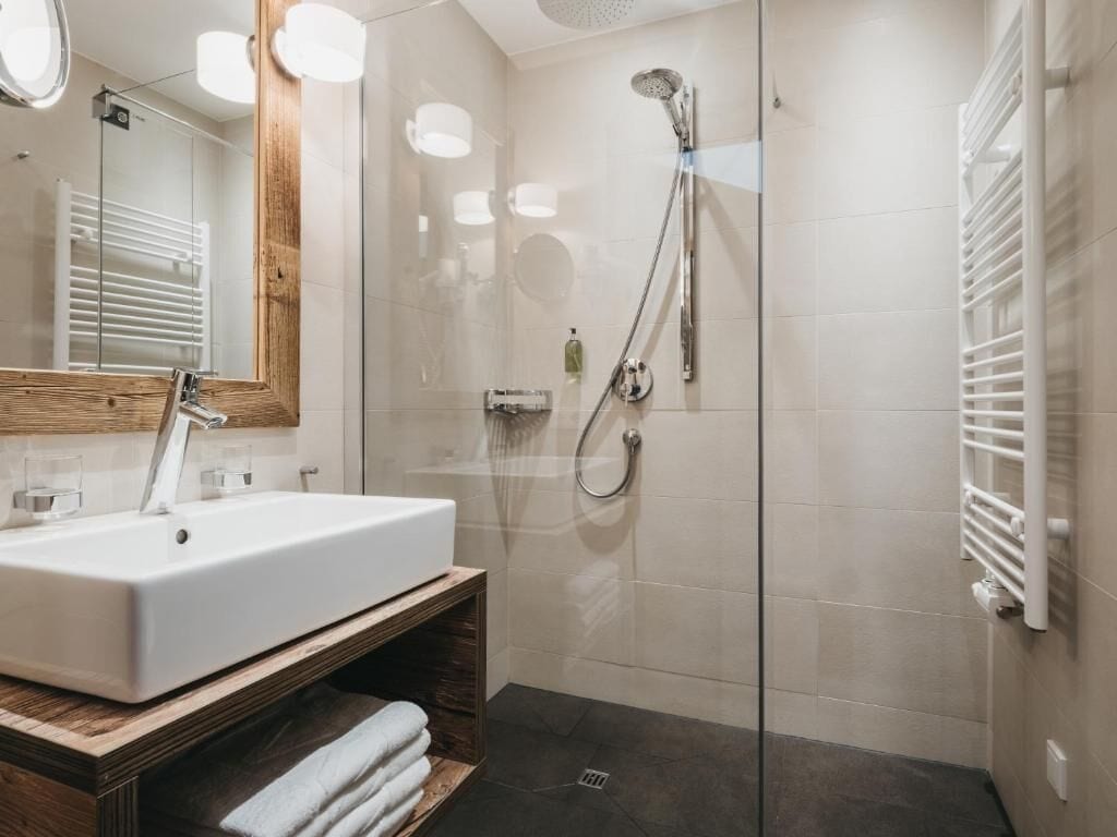 A modern bathroom with a glass-enclosed shower, a white sink, and a wooden vanity.