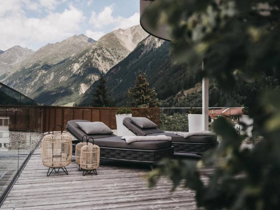 A rooftop terrace with lounge chairs and wicker tables, overlooking a mountainous landscape.