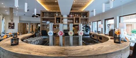 Un espace bar doté d’un comptoir en bois, de plusieurs robinets et d’étagères remplies de bouteilles et de verres.