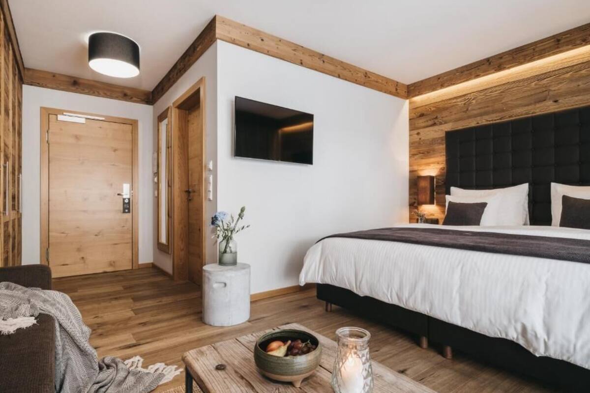 Un dormitorio moderno con techo de madera, una cama con ropa de cama blanca, una mesita de noche con una vela y un televisor montado en la pared.
