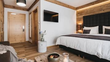 Une chambre moderne avec un plafond en bois, un lit recouvert d’une literie blanche, une table de chevet avec une bougie et un téléviseur fixé au mur.