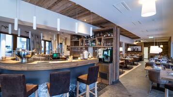 A modern bar area with a wooden ceiling, bar stools, and a variety of bottles and glasses on shelves.