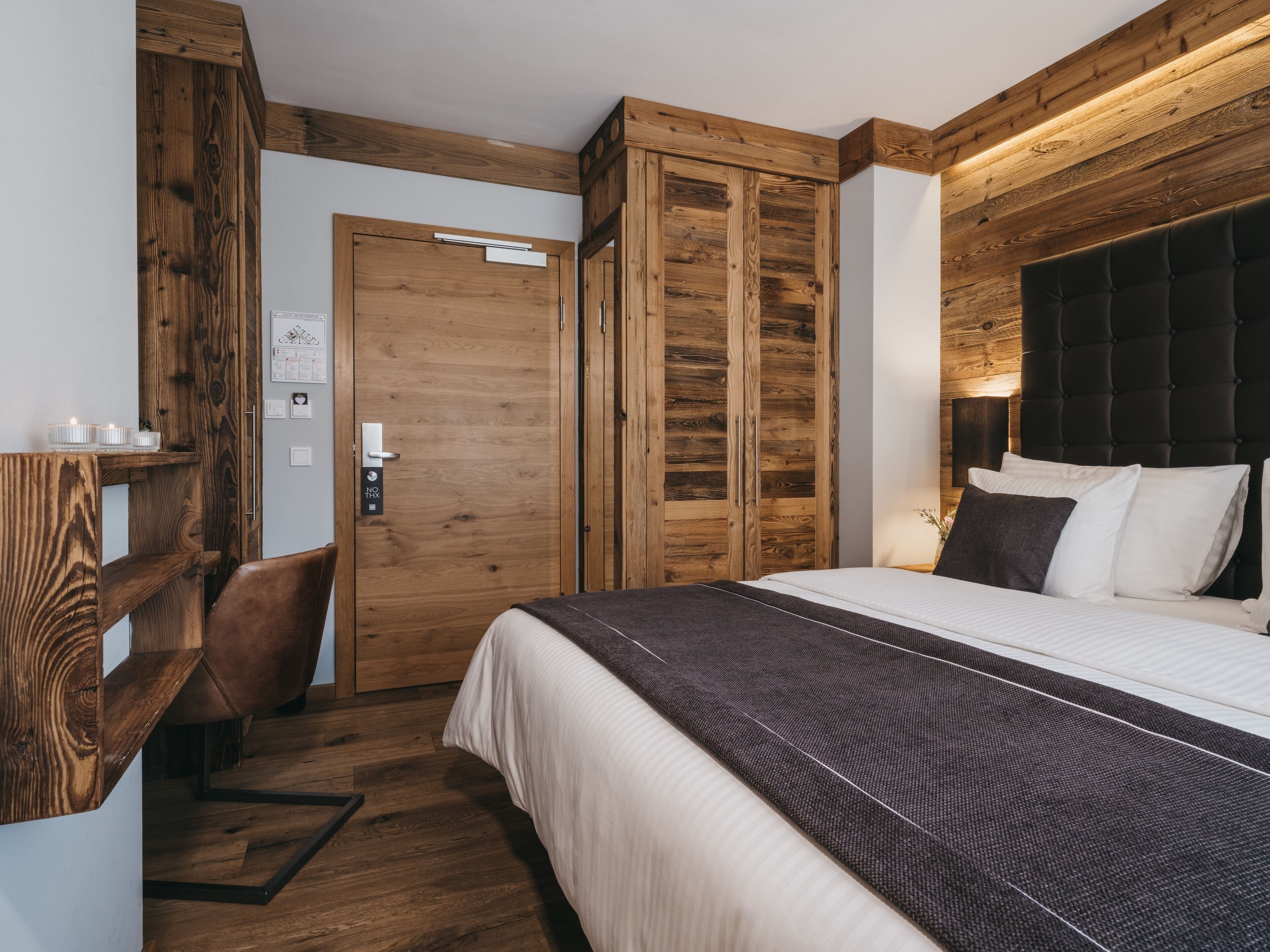 A bedroom with a bed, wooden wardrobe, and a desk with a chair.