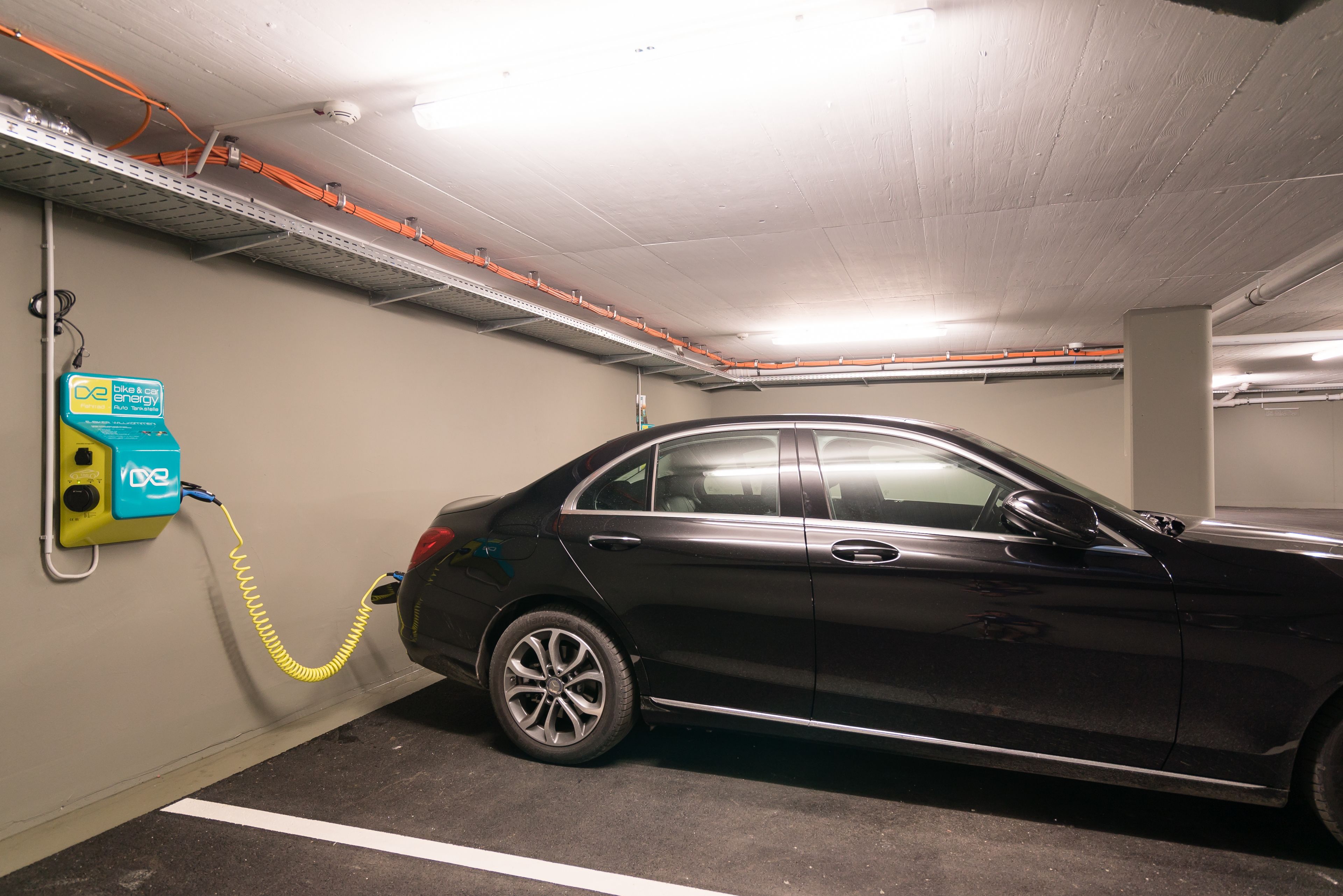 Une voiture en cours de recharge dans un parking, avec des câbles électriques apparents et une borne de recharge.