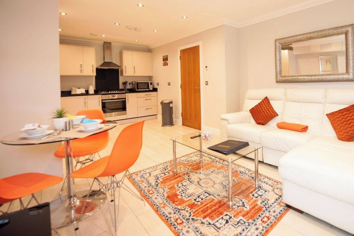 Uma sala de estar moderna com um sofá branco, poltronas laranja e uma mesa de centro de vidro.