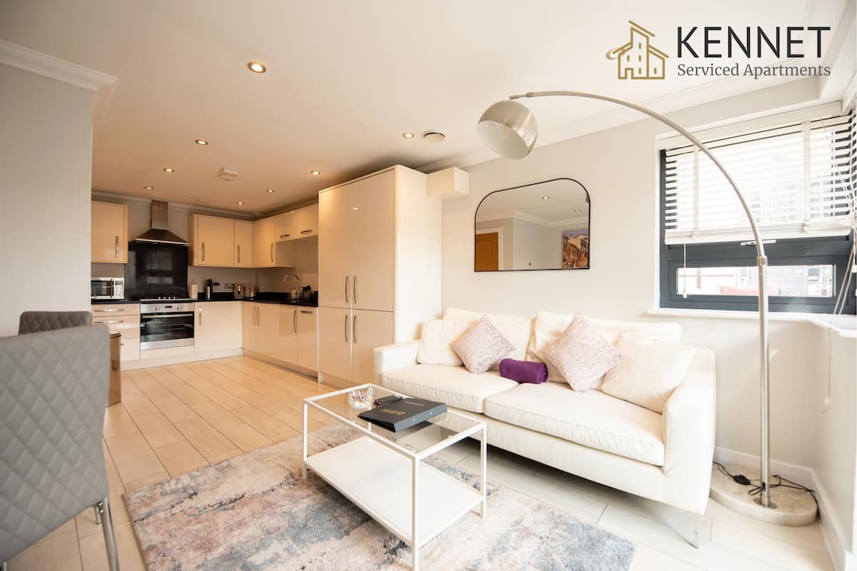 Apartamento moderno com sala de estar, cozinha e área de jantar. Apresenta um sofá branco, uma mesa de centro de vidro e um espelho grande.