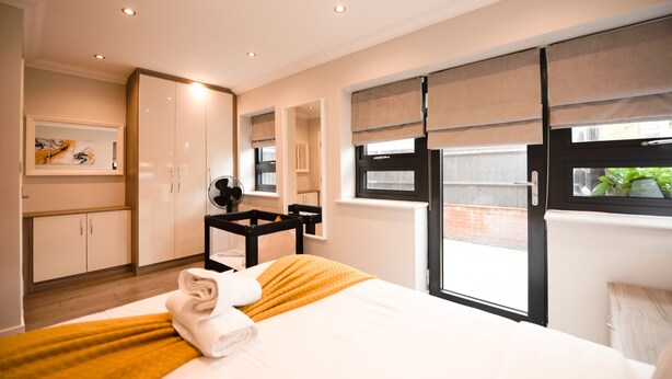 A modern hotel room with a large bed, a desk, and a view of the outside. - Malthouse Court (Reading)