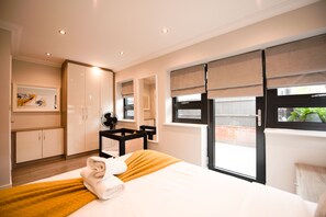 A modern hotel room with a large bed, a desk, and a view of the outside. - Malthouse Court (Reading)