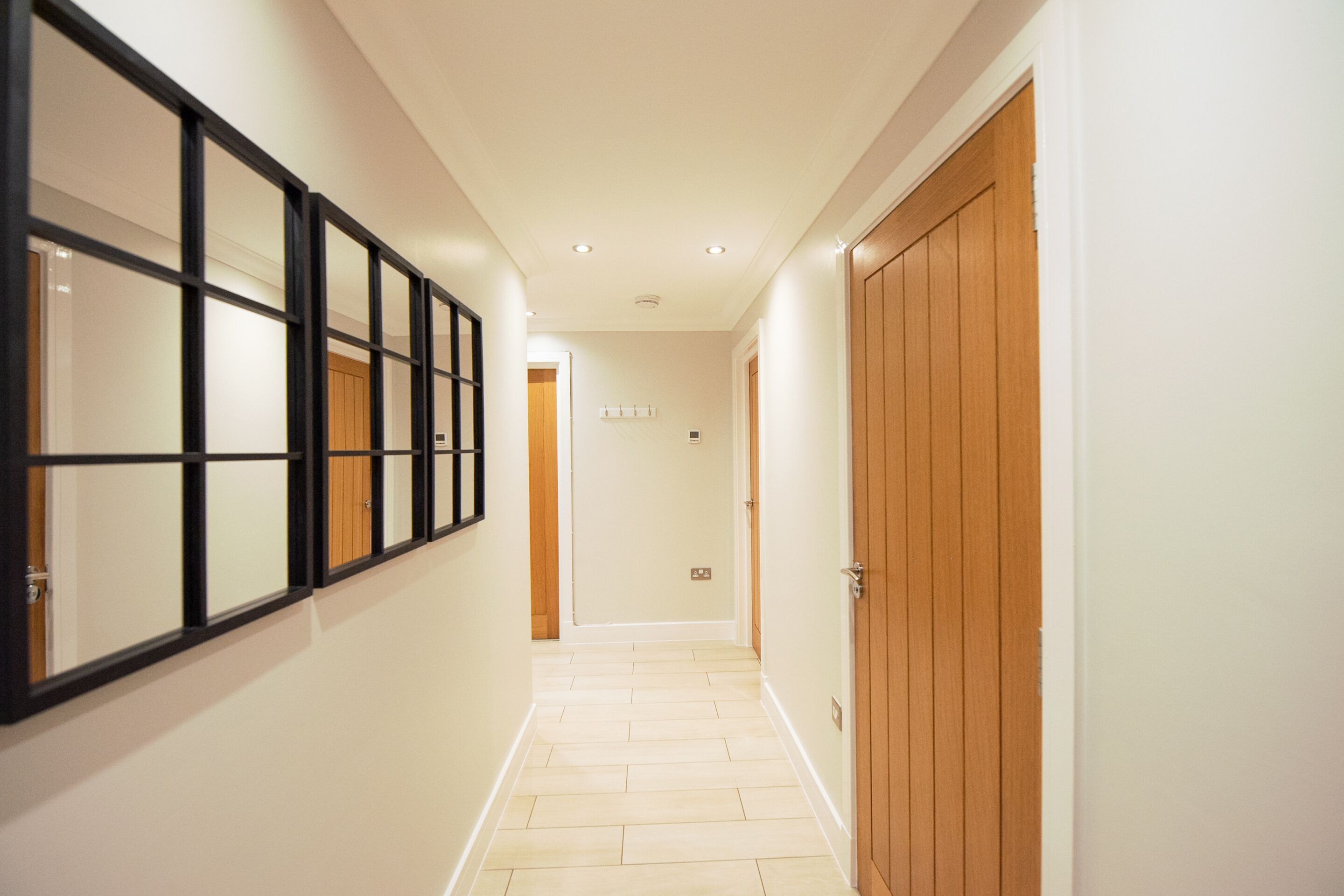 A hallway with a wooden door, a black-framed window, and a light-colored floor.