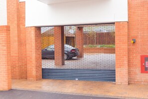 A brick building with a closed garage door and a red fire alarm box. - Malthouse Court (Reading)