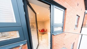 A view of a red brick building with a sliding glass door leading to a room with a red table and chairs. - Malthouse Court (Reading)