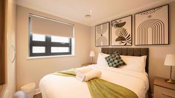 A hotel room with a bed, a window with blinds, a bedside table with a lamp, and wall art.
