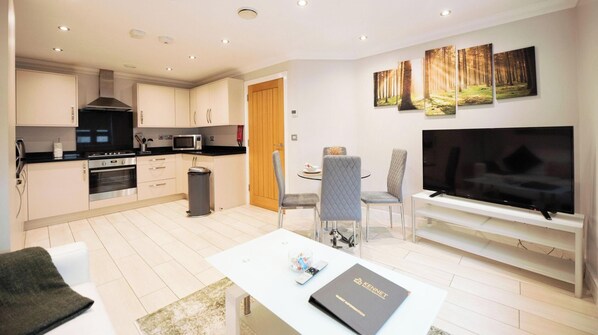 A modern kitchen with stainless steel appliances, a dining area with a table and chairs, and a flat-screen TV mounted on the wall. - Malthouse Court (Reading)