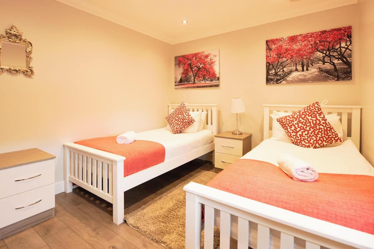 Quarto com duas camas de solteiro, uma mesinha de cabeceira, cômoda e duas pinturas na parede.
