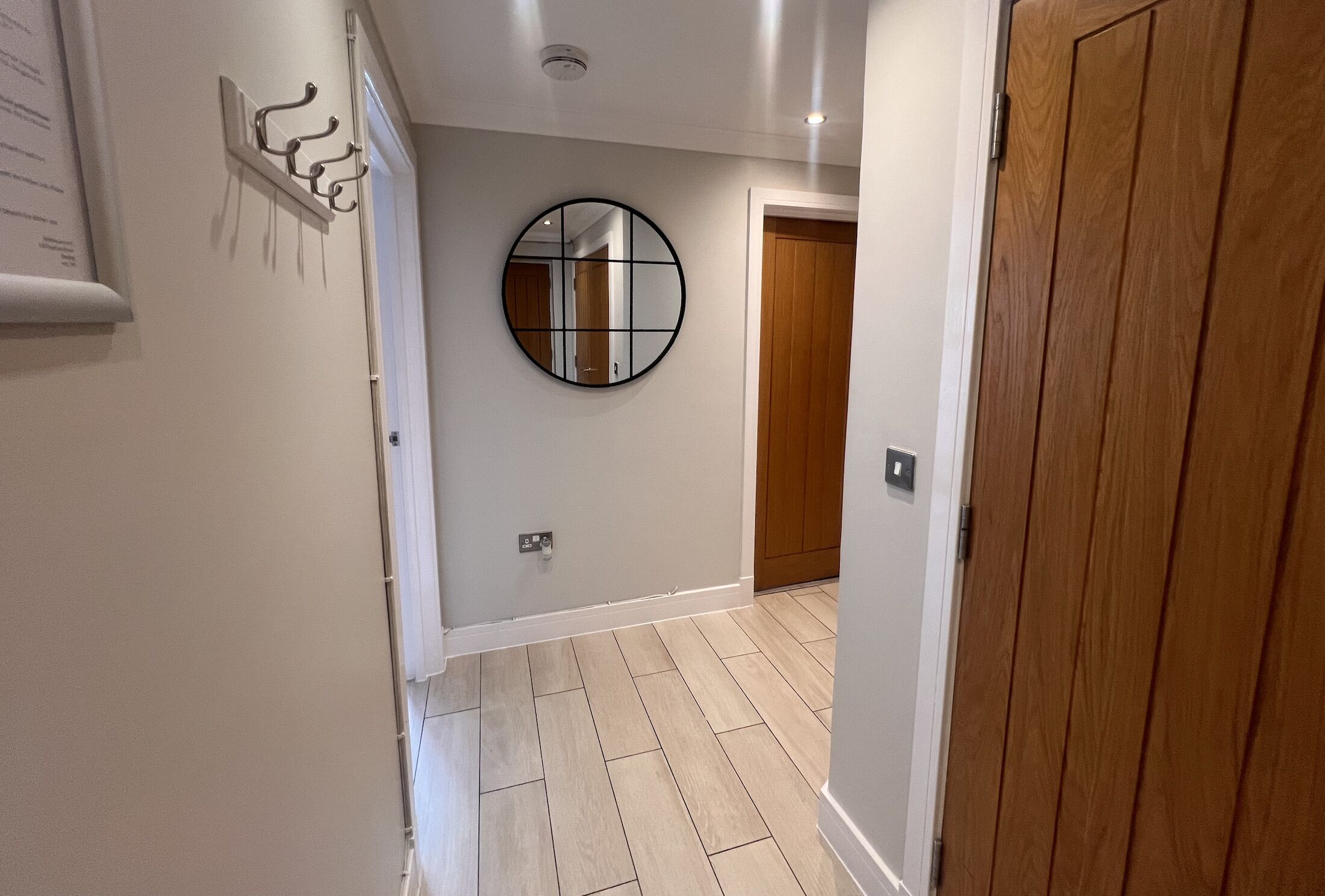 A hallway with a wooden door, a round mirror, and a wall-mounted light fixture.