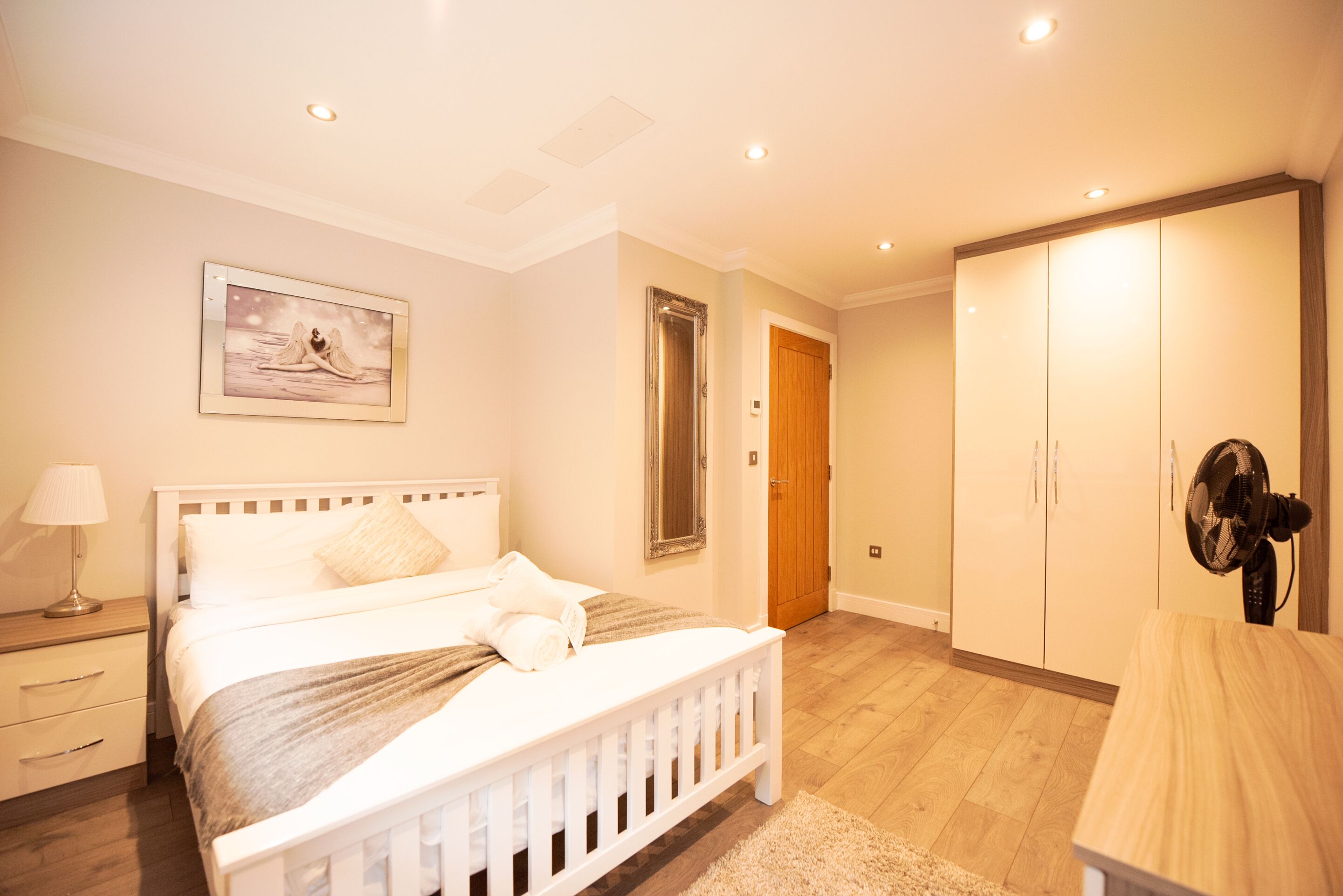 Een slaapkamer met een bed, nachtkastje, lamp en een kledingkast.